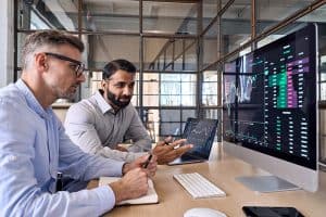 Two diverse business professionals discussing charts research reports growth using pc computer looking at screen analyzing investment strategy, financial risks