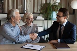 Happy elderly married couple shaking hands with a professional lawyer over a document